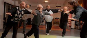 een groep oudere mannen staat op 1 been en probeert het evenwicht te houden