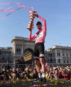 Tom Dumoulin in het roze tijdens de giro d'italia, hij staat op een podium en houdt de trofee omhoog