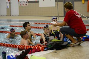 een coach legt jonge zwemmers iets uit aan de rand van het zwembad