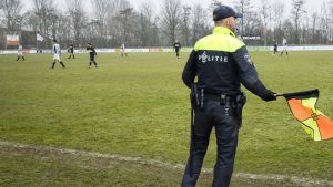 een politieagent staat als grensrechter langs de lijn bij het voetbalveld