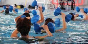 mensen in een zwembad aan het sporten met gewichten in hun handen