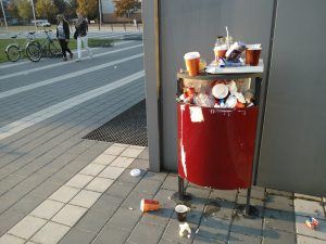 Een prullenbak op straat die overvol is, afval staat er op en naast op stra